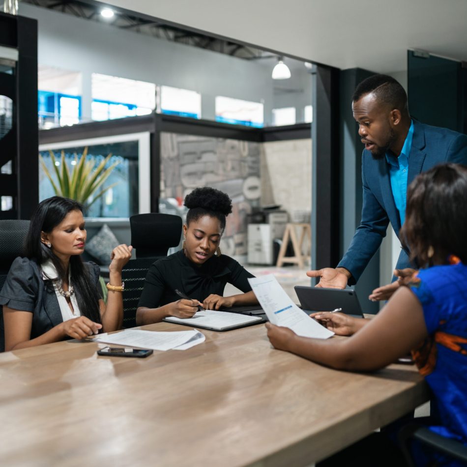 Young African businessman talking with a diverse team of colleagues during a meeting around a table in an office boardroom